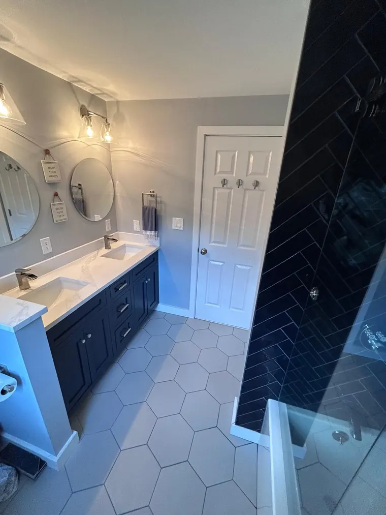 Navy blue subway tile shower next to a double vanity on a hexagon tile floor