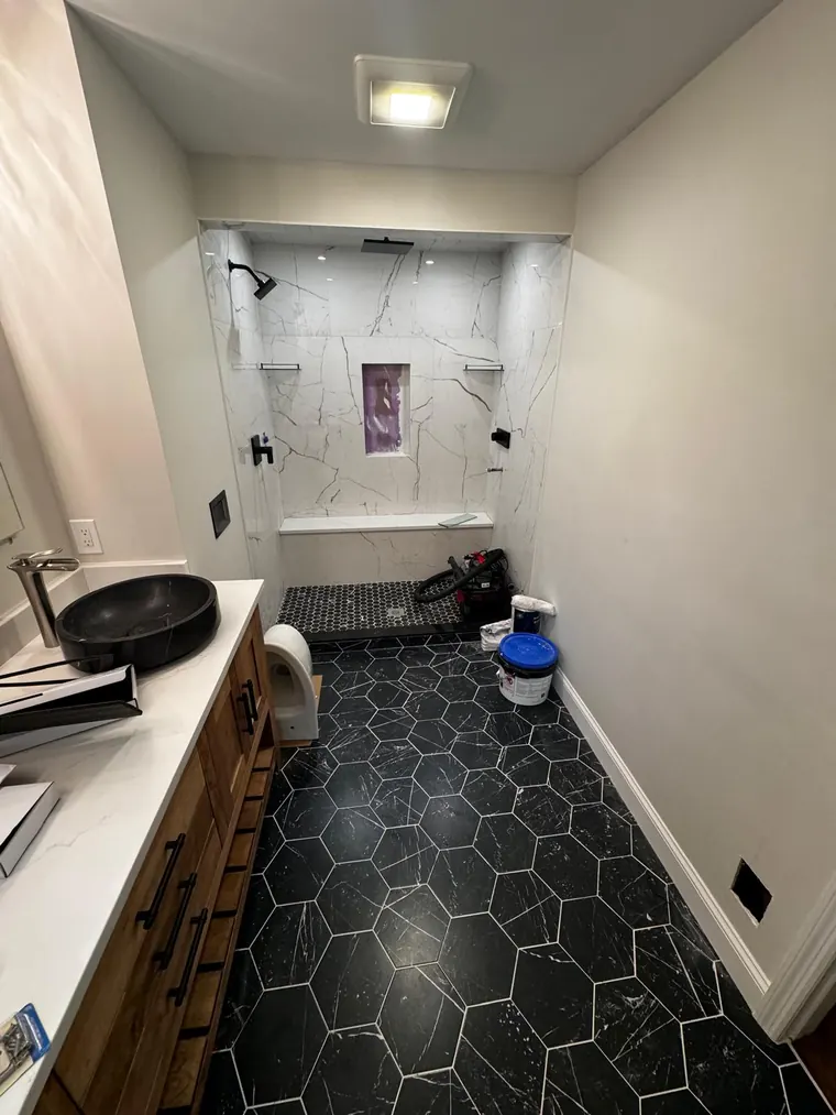 Black hexagon floor tile with a vessel sink and a wood vanity